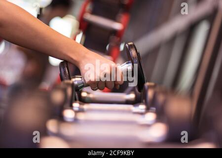 Seitenansicht des anonymen Crop-Athleten, der Hantel aus Metall nimmt Gestell mit Geräten während des Trainings im modernen Fitnessraum Stockfoto