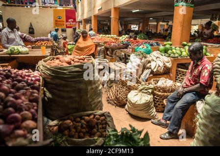 Jinja, Uganda - September,30:Verkäufer verkaufen Kartoffeln in Säcken Zwiebeln Gemüse Wassermelonen Früchte, während Frau entlang Reihen gehen und Einkäufe machen Stockfoto