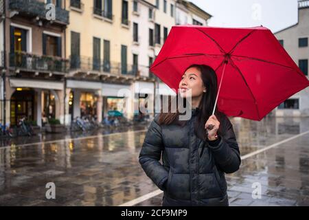 Junge asiatische weibliche Reisende in warmer Kleidung Sightseeing mit roten Regenschirm mit alten Gebäuden auf verschwommenem Hintergrund bei Padova at Italien Stockfoto