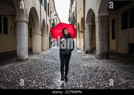 Junge asiatische weibliche Reisende in warmer Kleidung Sightseeing mit roten Regenschirm mit alten Gebäuden auf verschwommenem Hintergrund bei Padova at Italien Stockfoto