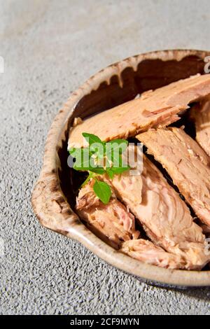 Nahaufnahme von einigen Stücken spanischer Bonito en aceit, einem Makrelenartigen Fisch in Öl, in einem Steingutteller, auf einer strukturierten grauen Oberfläche Stockfoto