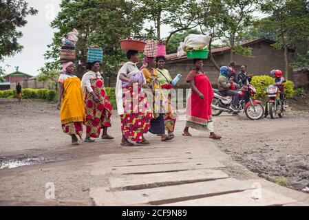 Ruanda, Afrika - 14. Dezember 2019: Afroamerikanische Frauen, die auf Köpfen Schüsseln tragen, gehen auf der Straße der örtlichen armen Stadt Stockfoto