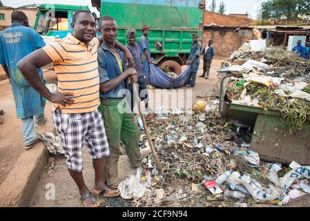 Ruanda, Afrika - 14. Dezember 2019: Afroamerikanischer Rüde in Casual Wear umarmt ernsthaften schwarzen Kerl für Schulter Müllabfuhr auf der Straße des lokalen Dorfes Stockfoto