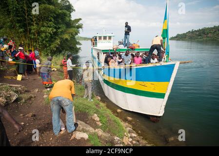 Ruanda, Afrika - 14. Dezember 2019: Kleines Schiff mit einer Gruppe von schwarzen Leuten, die im Wasser des Flusses mit tropischen Grüns herum vertäut sind Stockfoto