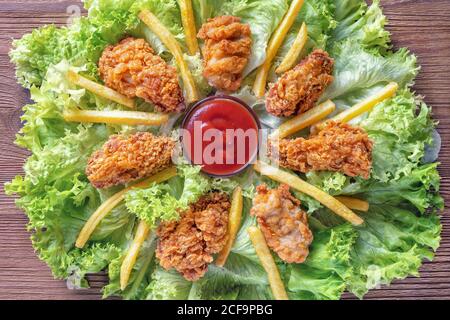Leckere knusprige gebratene Hähnchenflügel auf grünem Salat, Nahaufnahme Stockfoto