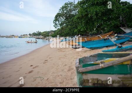 Tangalle, Sri Lanka - 28. Juli 2019: Leerer Sandstrand mit bunten Holzbooten und grünen exotischen Pflanzen bei bewölktem Wetter Stockfoto