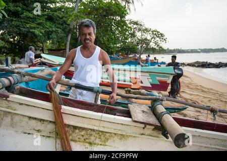 Tangalle, Sri Lanka - 28. Juli 2019: Alte ethnische Fischer in weißen hellen Kleidung Vorbereitung Fischernetz auf dem Boot Stockfoto