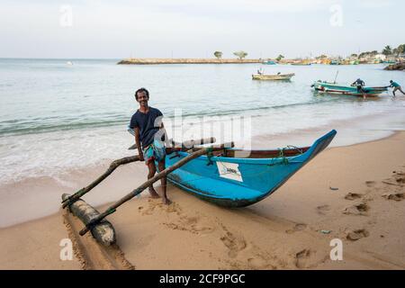 Tangalle, Sri Lanka - 28. Juli 2019: Ethnische junge Fischer in Freizeitkleidung mit traditionellen Boot im Meer Stockfoto