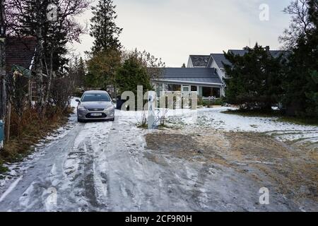 Graues Elektroauto auf verschneiten Hof in der Nähe Landhaus unter Schöner Garten im Winter Stockfoto