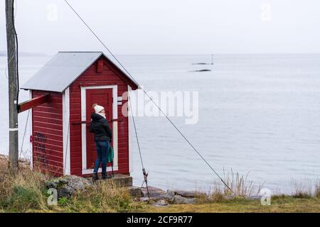 Frau in warmen Kleidern am Meer kleine rote Holzhütte genießen Schönheit der nördlichen Landschaft in Tromso, Norwegen Stockfoto