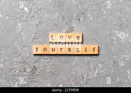 Liebe dich selbst Wort auf Holzblock geschrieben. Love Yourself Text auf Zementtisch für Ihr Design, Draufsicht Konzept. Stockfoto