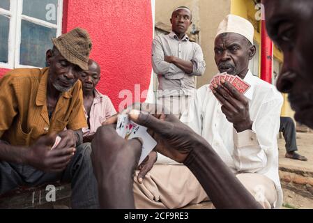 Uganda - November, 26 2016: Gruppe von schwarzen Männern in legerer Kleidung spielen Kartenspiel, während sie um die Bank auf der Straße der Stadt sitzen Stockfoto