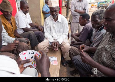 Uganda - November, 26 2016: Gruppe von schwarzen Männern in legerer Kleidung spielen Kartenspiel, während sie um die Bank auf der Straße der Stadt sitzen Stockfoto
