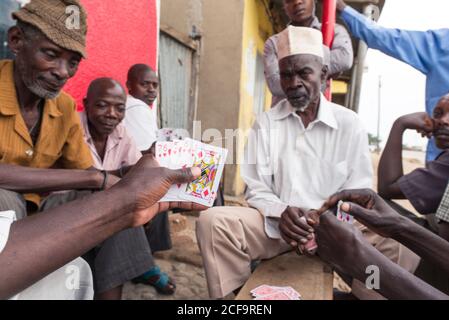 Uganda - November, 26 2016: Gruppe von schwarzen Männern in legerer Kleidung spielen Kartenspiel, während sie um die Bank auf der Straße der Stadt sitzen Stockfoto