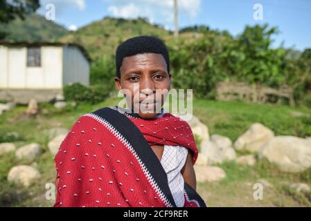 Uganda - November, 26 2016: Freundliche reife schwarze Hündin in traditioneller Stammeskleidung, die an sonnigen Tagen im Dorf vor die Kamera schaut Stockfoto
