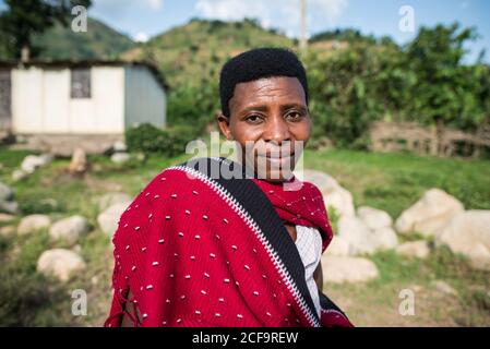Uganda - November, 26 2016: Freundliche reife schwarze Hündin in traditioneller Stammeskleidung, die an sonnigen Tagen im Dorf vor die Kamera schaut Stockfoto