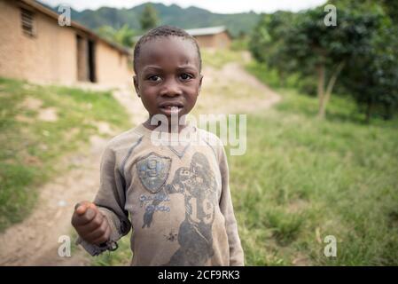 Uganda - November, 26 2016: Afrikanisches Kind, das auf einer schmutzigen Straße außerhalb des Dorfes vor der Kamera steht Stockfoto