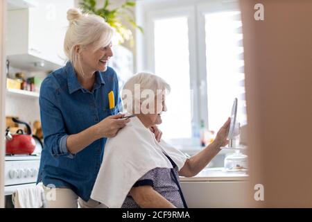 Frau schneidet ihrer älteren Mutter zu Hause die Haare Stockfoto