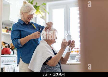 Frau schneidet ihrer älteren Mutter zu Hause die Haare Stockfoto