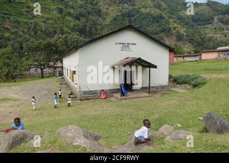 Uganda - 26. November 2016: Kirchenschule am grasbewachsenen Hang mit hohen grünen Bäumen und spielenden Kindern Stockfoto