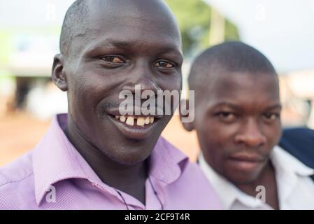 Uganda - November, 26 2016: Freundliche junge schwarze Männer, gut gekleidet und mit Blick auf die Kamera, während sie mitten in einer Straße im Dorf stehen Stockfoto