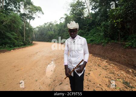 Uganda - November, 26 2016: Freundlicher, reifer schwarzer Mann, gut gekleidet mit Cowboyhut, der die Kamera anschaut, während er auf der Feldweg-Straße im Dorf steht Stockfoto