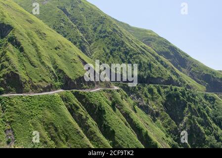 Von oben herrlicher Blick auf leere Serpentinenstraße auf grün Grashang gegen nebeliges Tal und bewaldete Berge in Georgien Stockfoto