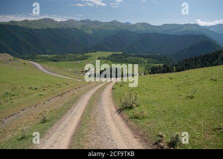 Blick auf die Straße, die zum erstaunlichen Dorf Omalo auf Ebene gegen grün nebligen Tal und bewaldeten Bergen in Georgien Im sonnigen Sommertag Stockfoto