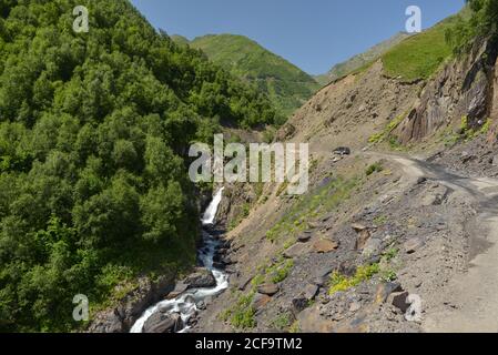 Von oben herrliche Aussicht auf den schmalen Wasserbach Fluss und Grüne grasbewachsene Hügel gegen nebeliges Tal und bewaldete Berge in Georgien Stockfoto