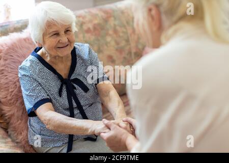 Weibliche Hausfrau Unterstützung alte Frau zu stehen aus Das Sofa im Pfleheim Stockfoto