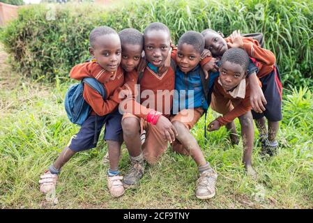 Uganda - November, 26 2016: Afrikanische Kinder mit Schuluniform, die sich umarmen, während sie die Kamera auf einer grünen Landschaft sehen Stockfoto