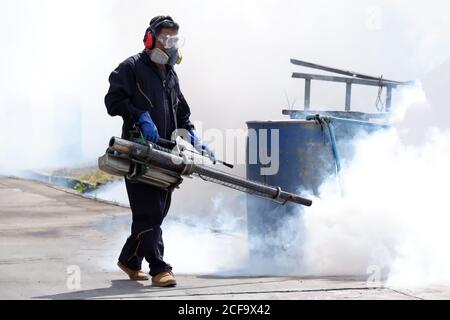 Outdoor-Gesundheitsarbeiter in Schutzkleidung mit chemischen Nebelmaschinen, um Mücken zu töten. Stockfoto