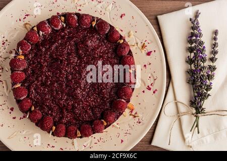 Von oben saftiger Obstkuchen mit Himbeeren auf weißem Teller Auf Holz Hintergrund mit Lavendel Bouquet dekoriert Stockfoto