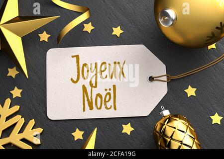 Weihnachten - Geschenk-Tag mit der französischen Frohen Weihnachtsbotschaft 'Joyeux Noël' auf schwarzem Steingrund mit goldfarbenen weihnachtsornamenten. Stockfoto