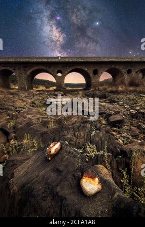 Felsiger Boden und alte Steinbrücke mit bunten Nachthimmel Mit Milchstraße und Sternen im Hintergrund Stockfoto