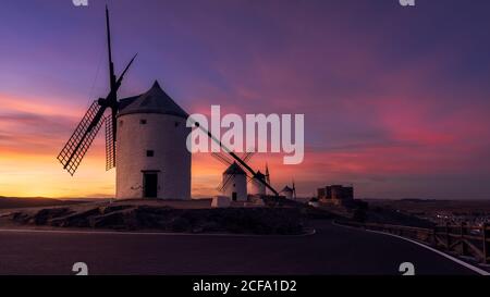 Alte Windmühlen auf felsigen Klippen in der Nähe mittelalterlichen Burg gegen wolkiger Sonnenuntergang Himmel auf dem Land Stockfoto