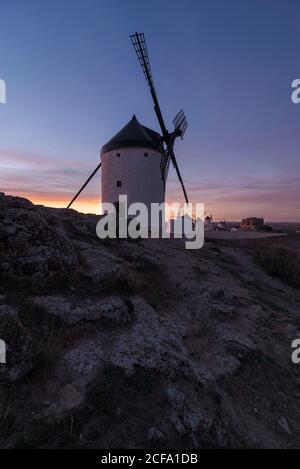 Alte Windmühle auf felsigen Klippen in der Nähe mittelalterlichen Burg gegen wolkiger Sonnenuntergang Himmel auf dem Land Stockfoto