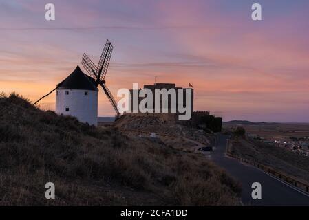 Alte Windmühle auf felsigen Klippen in der Nähe mittelalterlichen Burg gegen wolkiger Sonnenuntergang Himmel auf dem Land Stockfoto