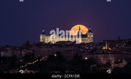 Wundervolle Landschaft des beleuchteten alten Palastes, der über der Stadt in gebaut wurde Bunte Nacht mit vollem roten Mond in Toledo Stockfoto