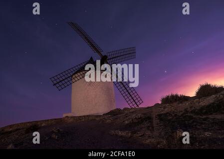 Alte Windmühle auf einer felsigen Klippe gegen bewölkten Sonnenuntergang Himmel auf dem Land Stockfoto