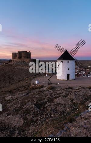 Alte Windmühle auf felsigen Klippen in der Nähe mittelalterlichen Burg gegen wolkiger Sonnenuntergang Himmel auf dem Land Stockfoto