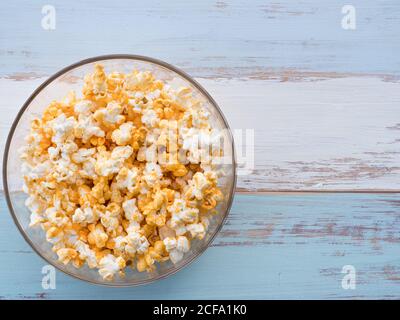 Popcorn in einer klaren Schale, runde Form auf einem Holzbrett aus blau und weiß Stockfoto