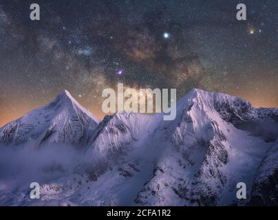 Tolle Aussicht auf die schneeweiße Bergkette in unglaublicher Nacht Sternenhimmel mit brechenden Strahlen der aufgehenden Sonne von hinten Berge im Winter Abend Stockfoto