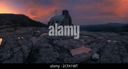 Malerische Landschaften von felsigen Klippen mit kleinen Steinhaus Lokalisierung In der Mitte der Berge gegen bewölkten Himmel bei Sonnenuntergang in Schöner Abend Stockfoto