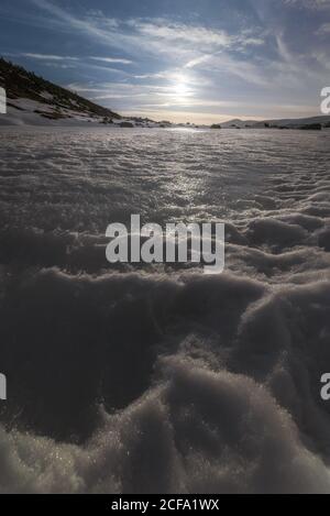 Majestätische Aussicht auf verschneiten gefrorenen See in der Mitte lokalisiert Verschneite bergige Gegend gegen wolkigen sonnigen Himmel im kühlen Winter Tag Stockfoto