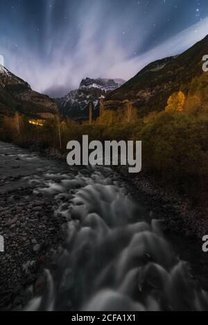 Fantastische Aussicht auf den unglaublichen Wasserfall in den Bergen, der über majestätischen Felsen fließt Landschaft mit grünen Bäumen und Bergkette, die gegen Wolken lokalisiert Nachthimmel Stockfoto