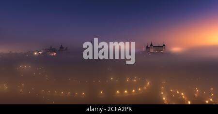 Von oben erstaunliche Landschaft der beleuchteten mittelalterlichen Stadt und Alcazar De Toledo Palast in nebligen bunten Sonnenaufgang Stockfoto