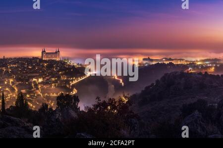 Von oben erstaunliche Landschaft der beleuchteten alten Alcazar de Toledo Burg über der Stadt in nebliger Dämmerung Stockfoto