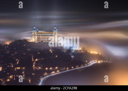 Von oben erstaunliche Landschaft der beleuchteten alten Alcazar de Toledo Burg über der Stadt in nebliger Dämmerung Stockfoto