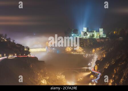 Von oben erstaunliche Landschaft der leuchtenden alten Burg und Brücke Im nebligen Berggelände bei Sonnenaufgang Stockfoto